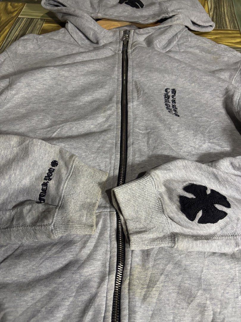 Chrome Hearts Grey Zip-Up Hoodie (Category: Hoodies) located in Manila. Submitted by thriftkibs (Listing ID 1469558459, Image 3). Description: - Brand: Chrome Hearts - Style: Grey cotton zip-up hoodie, casual streetwear staple - Details: Black cross patch on hood and left sleeve, vertical printed text branding on chest - Hardware: Signature dagger zipper pull - Fit: Ribbed cuffs and hem - Condition: Good, with some minor discoloration around the 