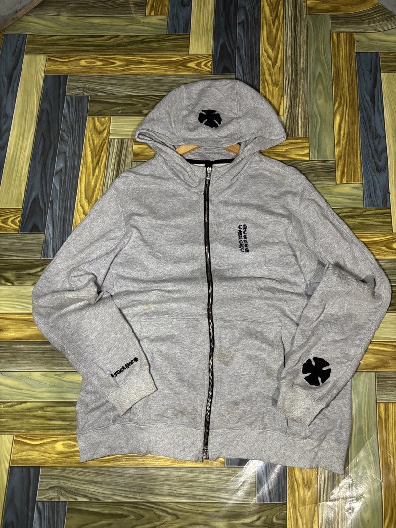 Chrome Hearts Grey Zip-Up Hoodie (Category: Hoodies) located in Manila. Submitted by thriftkibs (Listing ID 1469558459, Image 2). Description: - Brand: Chrome Hearts - Style: Grey cotton zip-up hoodie, casual streetwear staple - Details: Black cross patch on hood and left sleeve, vertical printed text branding on chest - Hardware: Signature dagger zipper pull - Fit: Ribbed cuffs and hem - Condition: Good, with some minor discoloration around the 