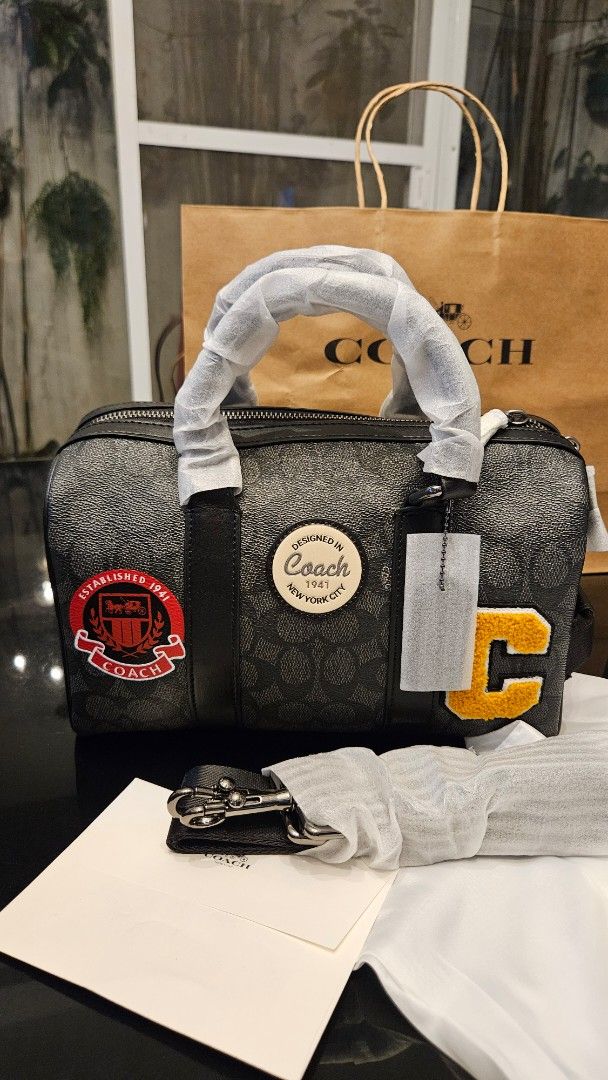 Coach Venturer (Category: Luxury Bags & Wallets) located in Rizal. Submitted by vanbdc24 (Listing ID 1469505301, Image 2). Description: - Authentic Coach Boston Bag in charcoal signature canvas - Black leather trim, dual top zip closure, and detachable shoulder strap - Features stylish yellow chenille letter C and red varsity shield patches with round Coach logo - Includes original dust bag and paper bag - Meet-ups and same-day delivery available