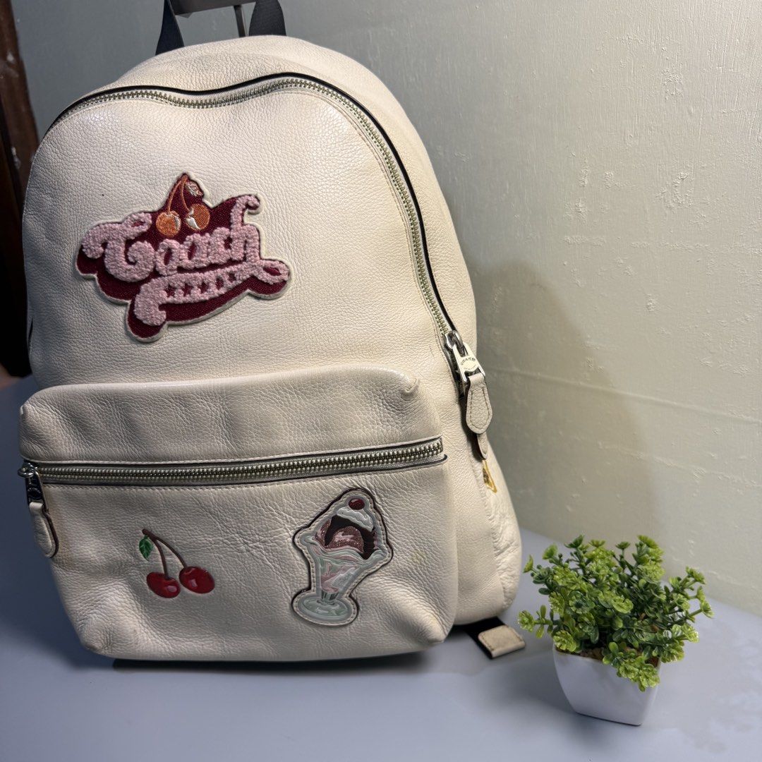 Coach White Leather Backpack with Patches (Category: Backpacks) located in Bago City. Submitted by g___shop (Listing ID 1469500212, Image 2). Description: - Brand: Coach - Material: White pebbled leather - Design: Features embroidered Coach logo, cherry, sundae, and yellow side patches - Compartments: Spacious main zip compartment and front pocket - Straps: Adjustable shoulder straps with top handle - Condition: Shows minor wear on the leather su
