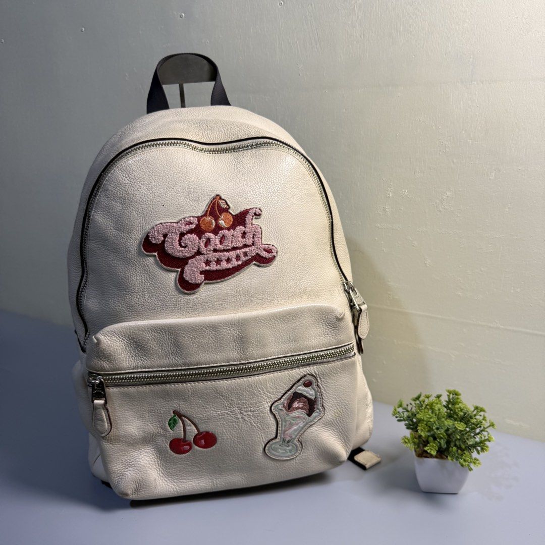 Coach White Leather Backpack with Patches (Category: Backpacks) located in Bago City. Submitted by g___shop (Listing ID 1469500212, Image 1). Description: - Brand: Coach - Material: White pebbled leather - Design: Features embroidered Coach logo, cherry, sundae, and yellow side patches - Compartments: Spacious main zip compartment and front pocket - Straps: Adjustable shoulder straps with top handle - Condition: Shows minor wear on the leather su