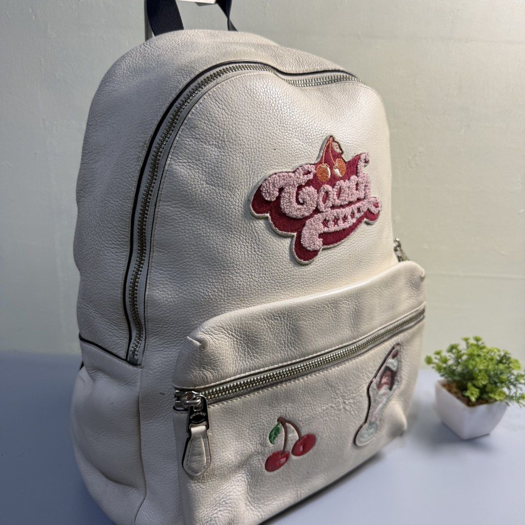 Coach White Leather Backpack with Patches (Category: Backpacks) located in Bago City. Submitted by g___shop (Listing ID 1469500212, Image 3). Description: - Brand: Coach - Material: White pebbled leather - Design: Features embroidered Coach logo, cherry, sundae, and yellow side patches - Compartments: Spacious main zip compartment and front pocket - Straps: Adjustable shoulder straps with top handle - Condition: Shows minor wear on the leather su