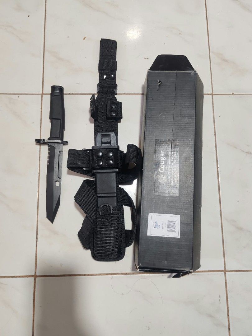 Cougar Tactical with Sheath and Box (Category: Hiking & Camping) located in Bacoor. Submitted by kuroochiii94695 (Listing ID 1469401600, Image 3). Description: - Brand: Cougar tactical kn i f e - Finish: Matte black with serrated spine - Handle: Rugged design with integrated guard - Sheath: Heavy-duty black nylon with multiple straps, belt loops, and modular attachments - Inclusions: Original Cougar-branded box with barcode - Condition: Sturdy, h
