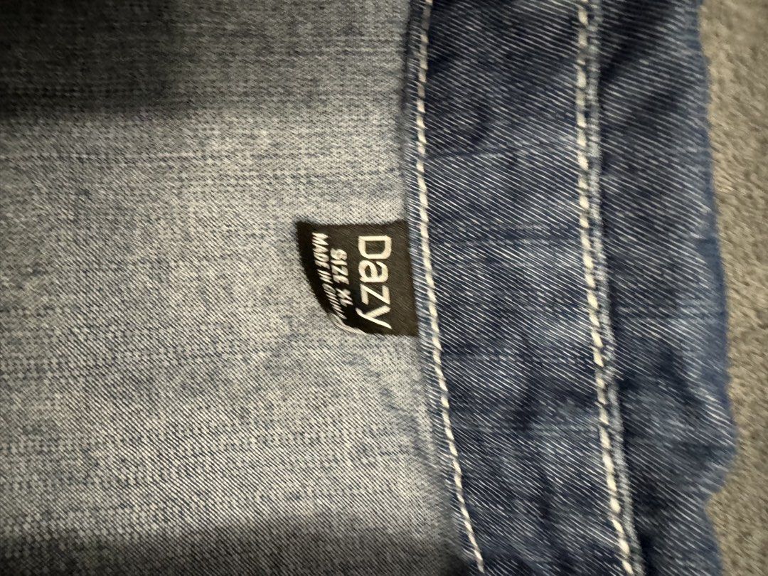 DAZY Denim Shirt Size XL (Category: Shirts) located in Taguig. Submitted by sqaumejada (Listing ID 1469572134, Image 2). Description: - Brand/Style: DAZY denim short sleeve shirt - Size: XL (Comfortable oversized fit) - Color/Wash: Dark blue wash with contrast white stitching - Design details: Polo collar, V-neck placket, and single chest pocket - Hem: Curved high-low hem with light trim.