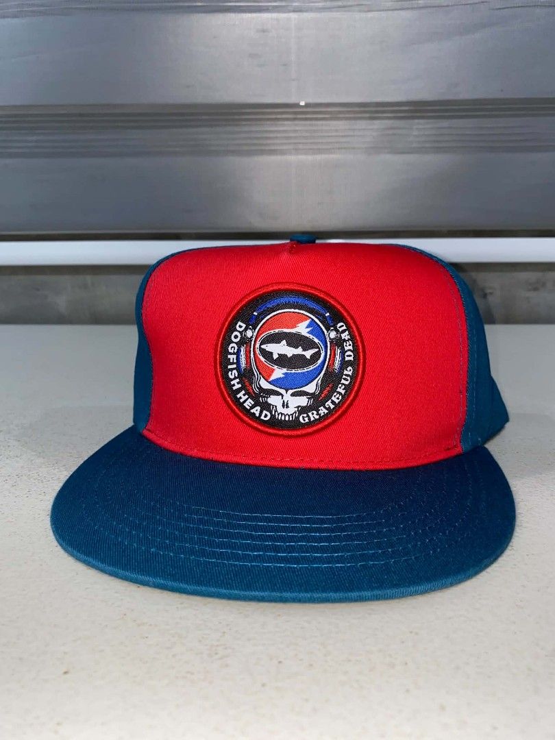 Dogfish Head x Grateful Dead Snapback Hat (Category: Caps & Hats) located in Baler. Submitted by mariokush193815 (Listing ID 1469453230, Image 1). Description: - Official Dogfish Head and Grateful Dead collaboration hat - Vibrant red front panel with contrasting dark blue brim and back panels - Eye-catching circular embroidered patch featuring the iconic skull, lightning bolt, and shark graphic - Adjustable plastic snapback closure for a customiz