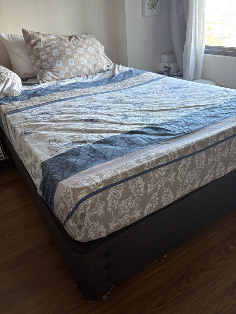 Double bed with mattress (Category: Bed Frames & Mattresses) located in Quezon City. Submitted by cattan7123 (Listing ID 1469542452, Image 2). Description: - Size: Queen size bed setup - Includes: Dark grey fabric base, comfortable mattress, and sturdy frame - Storage: Built-in pull-out drawers underneath for extra space - Bedding: Patterned bedsheets with blue and beige floral designs, pillows, and bolster included - Condition: Well-maintained, 