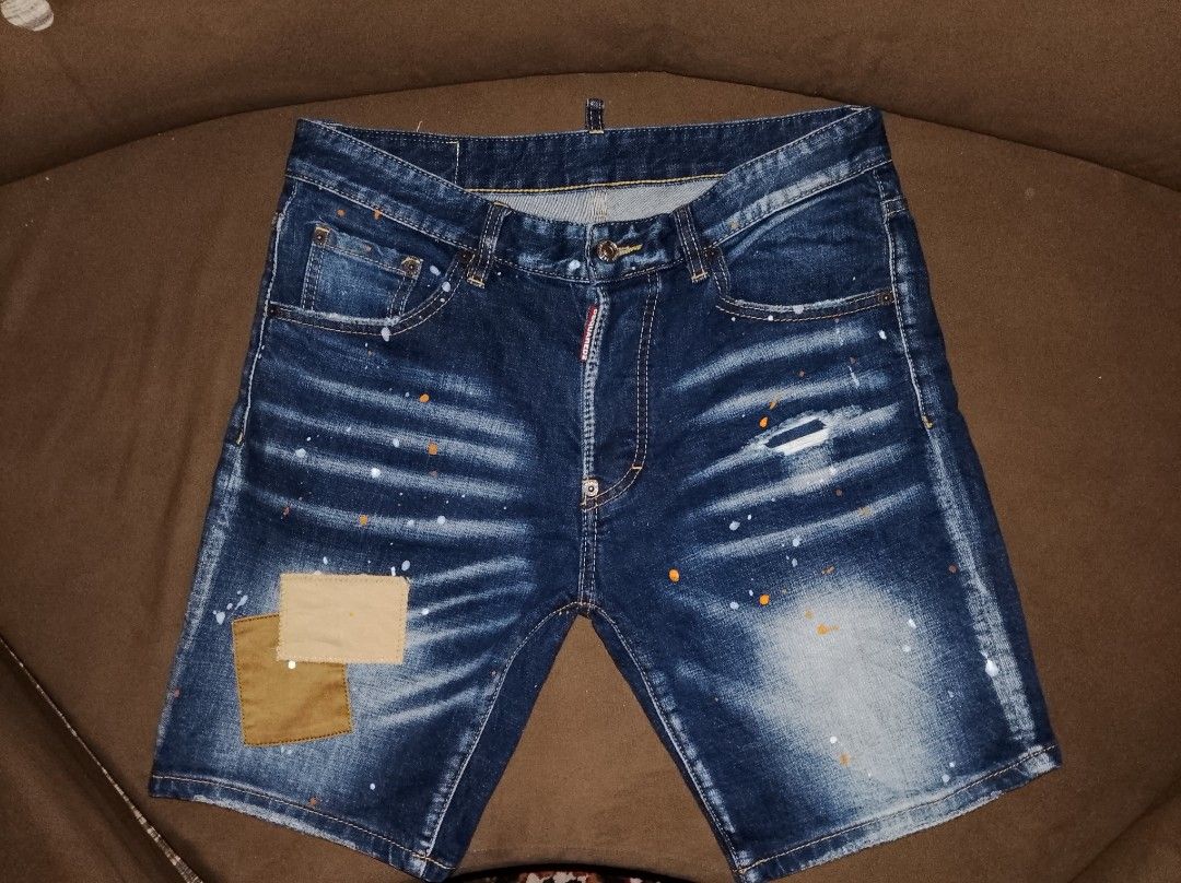 DSquared2 Distressed Paint Splatter Denim Shorts (Category: Activewear) located in Kapalong. Submitted by aliclothesfinds21 (Listing ID 1469566297, Image 1). Description: - Brand: DSquared2 - Style: Dark wash denim shorts with white and orange paint splatter details - Finish: Distressed with fading, whiskering, and a stylish repaired tear with fabric patches on the front right leg - Details: Branded button closure and back pocket tag - Condition: