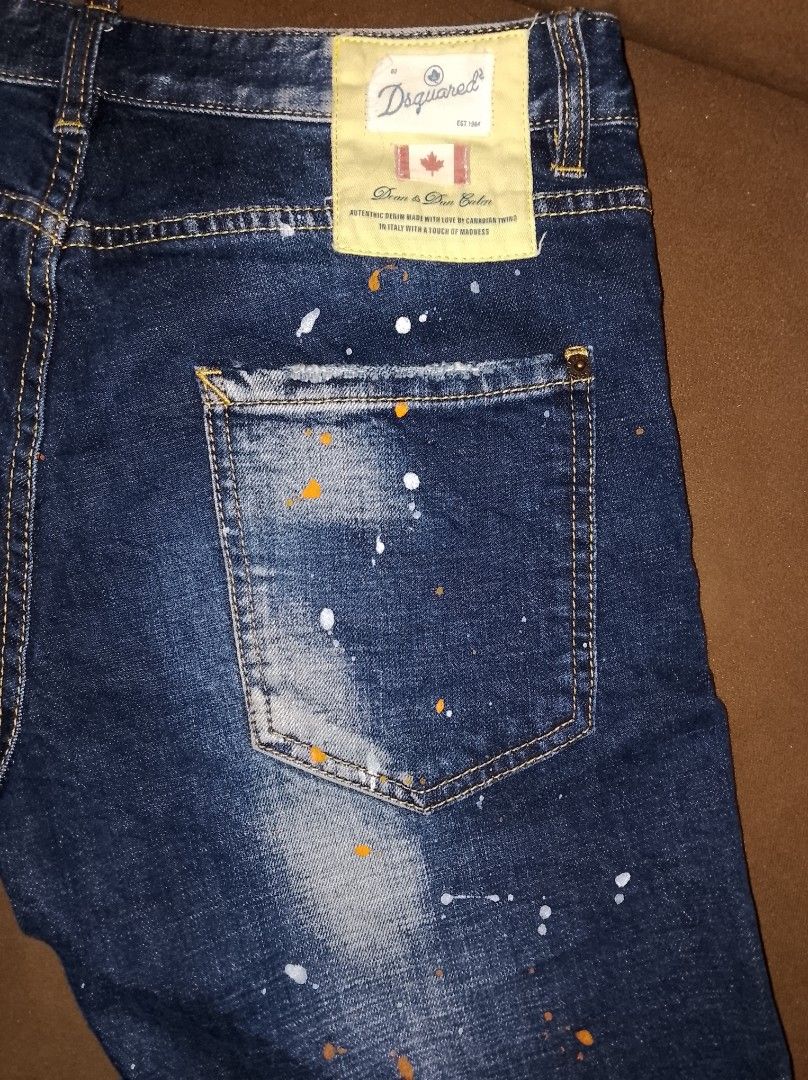 DSquared2 Distressed Paint Splatter Denim Shorts (Category: Activewear) located in Kapalong. Submitted by aliclothesfinds21 (Listing ID 1469566297, Image 3). Description: - Brand: DSquared2 - Style: Dark wash denim shorts with white and orange paint splatter details - Finish: Distressed with fading, whiskering, and a stylish repaired tear with fabric patches on the front right leg - Details: Branded button closure and back pocket tag - Condition: