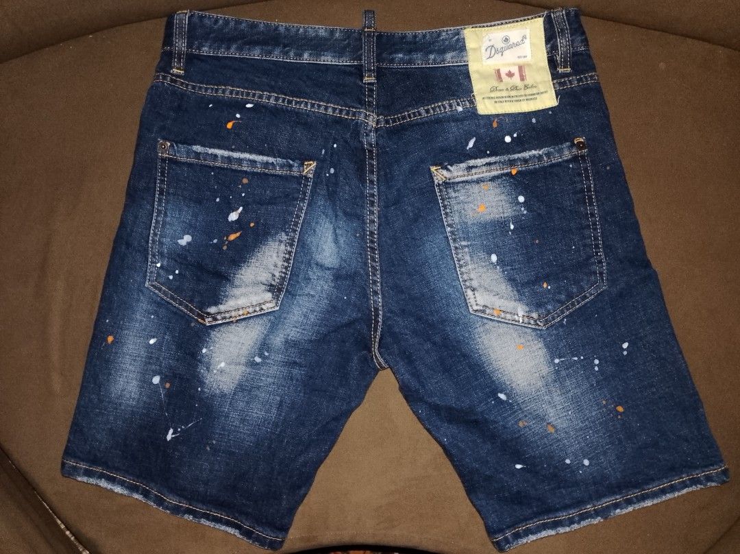 DSquared2 Distressed Paint Splatter Denim Shorts (Category: Activewear) located in Kapalong. Submitted by aliclothesfinds21 (Listing ID 1469566297, Image 2). Description: - Brand: DSquared2 - Style: Dark wash denim shorts with white and orange paint splatter details - Finish: Distressed with fading, whiskering, and a stylish repaired tear with fabric patches on the front right leg - Details: Branded button closure and back pocket tag - Condition:
