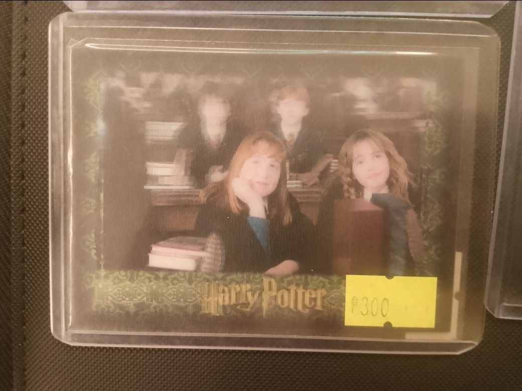 Harry Potter characters (Category: Raw Singles) located in San Juan City. Submitted by jim.jim7 (Listing ID 1469419731, Image 1). Description: - Item: Harry Potter trading card - Design: Characters sitting at a library desk with books, featuring a classic logo and green decorative border - Condition/Protection: Stored safely inside a clear protective top loader case - Note: Price sticker attached on the bottom right corner of the protective holde