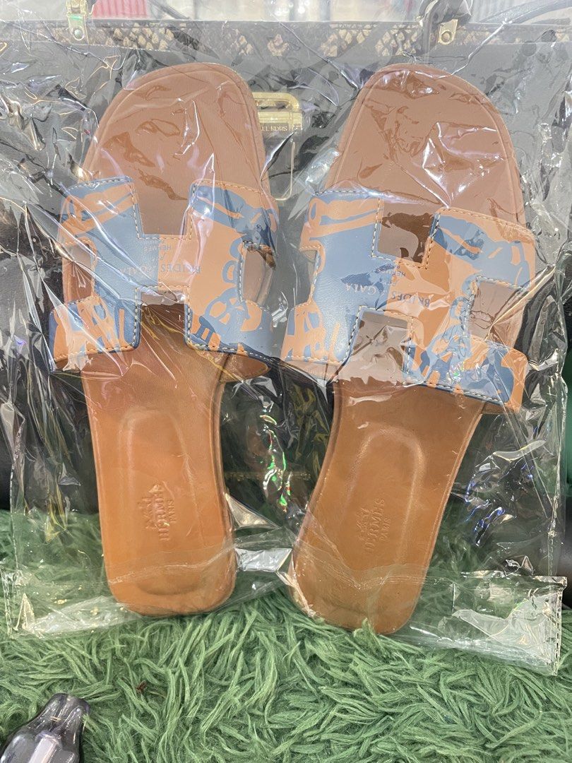 Hermes Orange Blue Printed Leather Sandals (Category: Flats & Sandals) located in Cainta. Submitted by mariss.luxx (Listing ID 1469469591, Image 1). Description: - Brand: Hermès - Style: Slip-on slide sandals - Color/Design: Tan brown base with blue and orange patterned 'H' strap - Features: Flat sole, stamped logo on insole heel - Condition: Brand new, sealed in original plastic packaging (never opened).