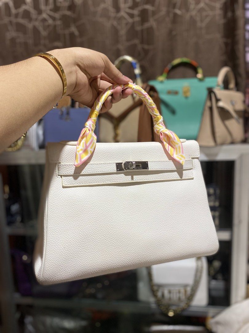 Hermes White Leather Kelly Bag with Twilly (Category: Luxury Bags & Wallets) located in Manila. Submitted by bvd9dwnrgf23014 (Listing ID 1469483382, Image 1). Description: - Style: Structured trapezoid handbag - Material: Premium white pebbled leather with silver hardware - Closure: Secure turn-lock closure - Detail: Comes with a chic pink, yellow, and white patterned silk twilly wrapped handle - Practicality: Flat bottom with protective feet and