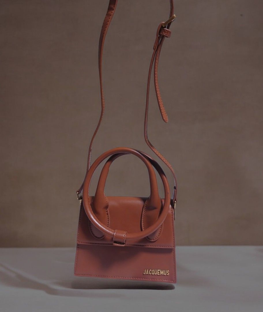 Jacquemus Brown Leather Handbag with Circular Handles (Category: Luxury Bags & Wallets) located in Umingan. Submitted by mrobvariety (Listing ID 1469468680, Image 2). Description: - Brand: Jacquemus - Material: Smooth brown leather with clean edge stitching - Design: Structured boxy shape with gold metallic front lettering - Handles: Double circular rigid top handles - Style: Compact, everyday luxury bag.