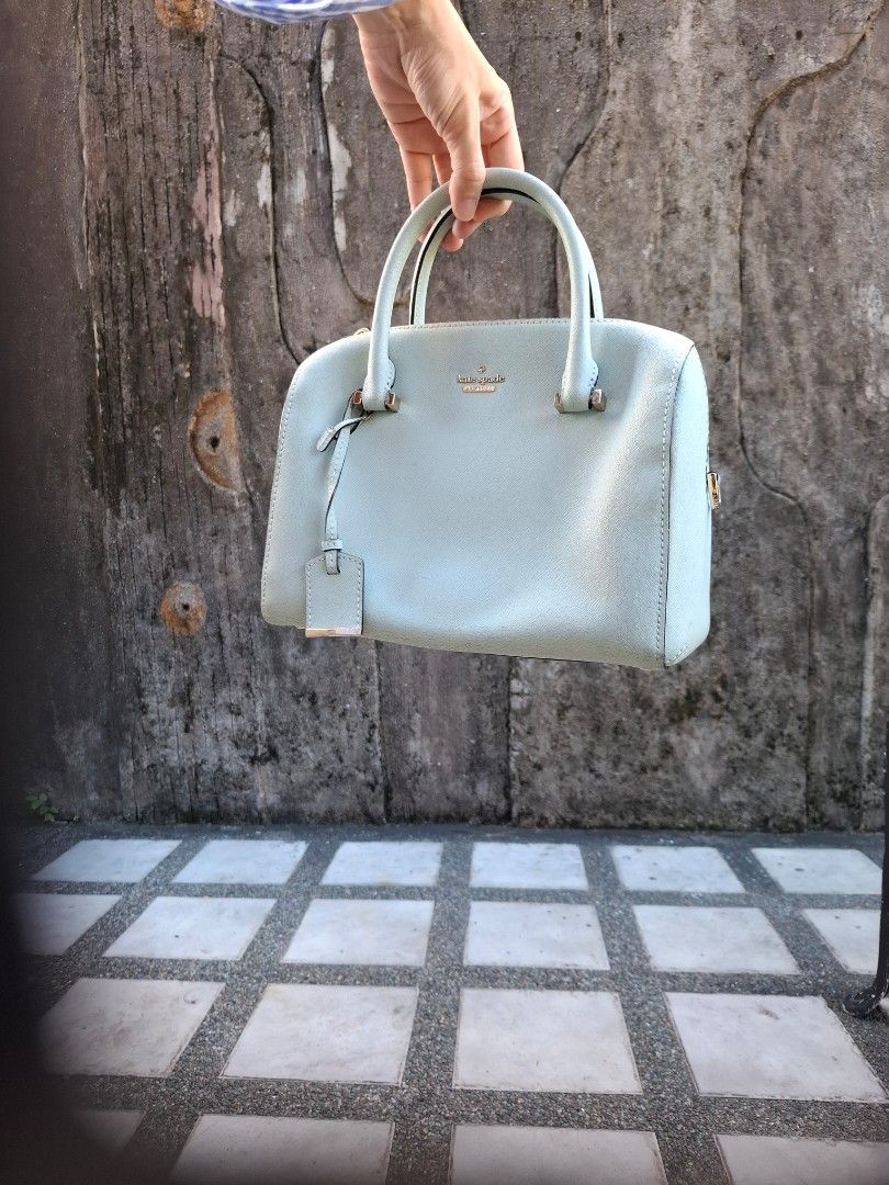 Kate Spade New York Light Blue Handbag (Category: Tote Bags) located in Makati City. Submitted by itemsforless2025 (Listing ID 1469482027, Image 2). Description: Light blue Kate Spade New York handbag with double top handles and gold hardware. Structured dome shape with a matching luggage tag accent. Zip top closure keeps your stuff secure. Clean textured leather exterior. Casual everyday bag holding keys, wallet, and phone easily. Some slight we