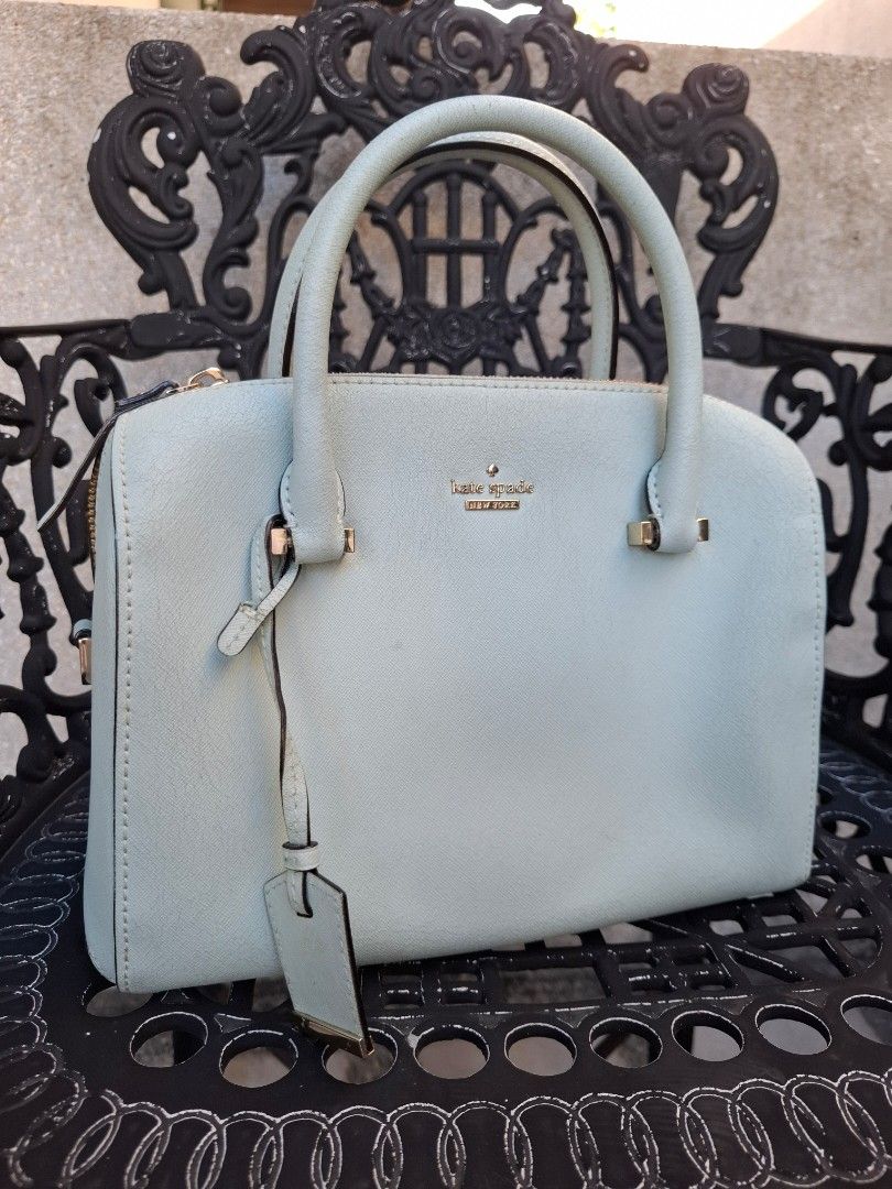 Kate Spade New York Light Blue Handbag (Category: Tote Bags) located in Makati City. Submitted by itemsforless2025 (Listing ID 1469482027, Image 1). Description: Light blue Kate Spade New York handbag with double top handles and gold hardware. Structured dome shape with a matching luggage tag accent. Zip top closure keeps your stuff secure. Clean textured leather exterior. Casual everyday bag holding keys, wallet, and phone easily. Some slight we