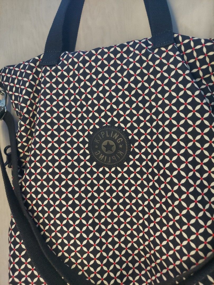 Kipling patterned tote bag with handles and strap (Category: Tote Bags) located in Quezon City. Submitted by never_a_clutter (Listing ID 1469512797, Image 2). Description: - Brand: Kipling - Design: Dark navy blue, white, and red geometric pattern with round front logo patch - Material: Durable fabric throughout - Carry Options: Sturdy dark blue fabric carry handles and an adjustable shoulder strap - Hardware: Silver-tone accents - Inclusion: Mat