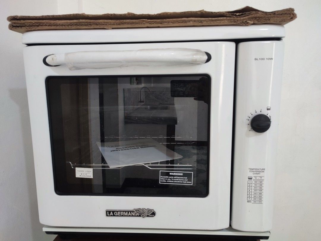 La Germania SL100 10W Electric Oven (Category: Ovens & Toasters) located in Bulacan. Submitted by Nekomimi12 (Listing ID 1469454633, Image 1). Description: - Brand: La Germania - Model: SL100 10W - Color: White - Control: Right-side rotary knob with temperature conversion chart - Door: Glass door with protective plastic on the handle - Interior: Clean black enamel cavity - Inclusions: Wire rack, baking tray, and instruction manual - Condition: Ex