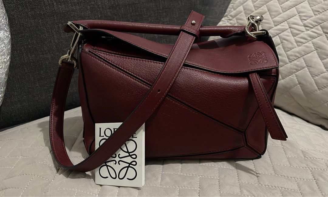 (RUSH) Loewe Puzzle Bag Burgundy Leather (Category: Luxury Bags & Wallets) located in Cavite. Submitted by cheetozjalapeeeeno (Listing ID 1467476271, Image 1). Description: Burgundy Loewe Puzzle bag in classic calfskin. Geometric panel design with silver-tone hardware. Removable shoulder strap with Anagram dice detail. Top handle and rear zip pocket. Cream herringbone canvas lining inside. Interior leather tag stamped Loewe Made in Spain. Structu