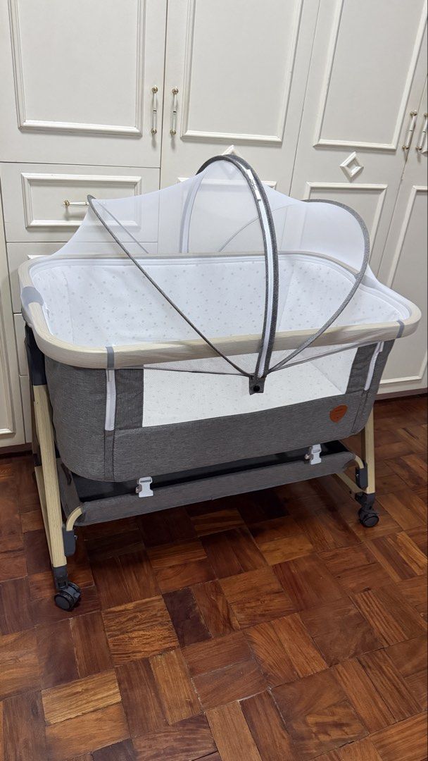 Mambo Baby Bedside Cot with Mosquito Net (Category: Cots & Cribs) located in Santa Cruz. Submitted by jlchua (Listing ID 1469509862, Image 2). Description: - Stylish grey Mambo bedside crib with chic wood-grain finish legs - Breathable mesh sides for optimal airflow and easy baby monitoring - Adjustable height levels to fit most beds securely - Includes a cozy mattress with a cute star-patterned lining - Detachable mosquito net canopy for added p