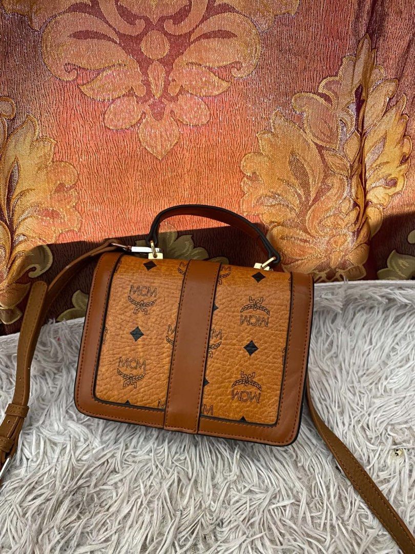 MCM Brown Monogram Crossbody Bag with Top Handle (Category: Luxury Bags & Wallets) located in Manila. Submitted by melissatua68314 (Listing ID 1469518097, Image 2). Description: - Brown MCM monogram crossbody bag - Structured silhouette with a chic top handle and adjustable shoulder strap - Secure gold-tone front lock closure - Clean fabric-lined interior featuring a convenient zipped middle compartment and slip pockets.