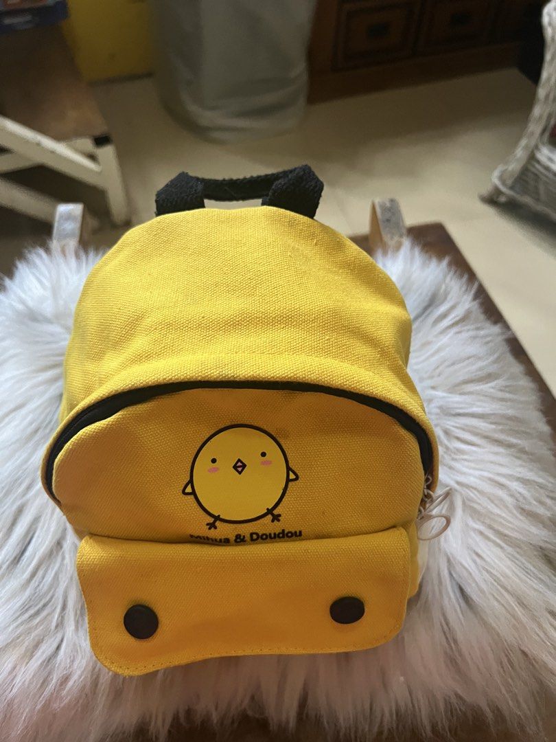 Mihua & Doudou Yellow Chick Backpack (Category: Backpacks) located in Rizal. Submitted by safecat_3c0d85 (Listing ID 1469431366, Image 1). Description: - Color: Bright Yellow - Material: Durable canvas - Design: Cute chick graphic with "Mihua & Doudou" text - Features: Front pocket with a clear display window under the flap, top grab handle, and black shoulder straps - Size: Compact and lightweight, perfect for daily casual outings and carrying s