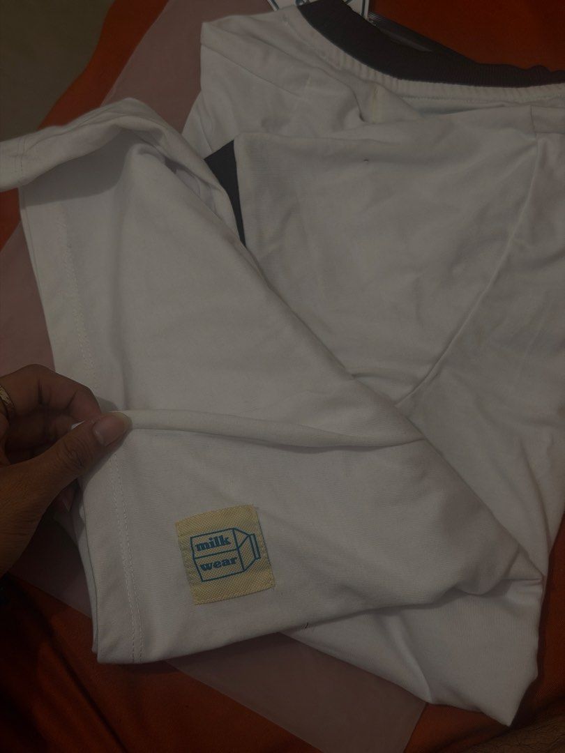 Milkwear Oat Milk Ringer Tee (Category: Tshirts & Polo Shirts ) located in Batangas. Submitted by jrxmy_ (Listing ID 1469410930, Image 3). Description: - Brand: Milkwear - Style: Ringer t-shirt in white with dark brown collar and sleeve trims - Design: 'Oat milk' graphic on chest and small milk carton patch near hem - Size: Small - Condition: Brand new, unworn, complete with cardboard hangtag - Packaging: Comes in original frosted ziplock packagi