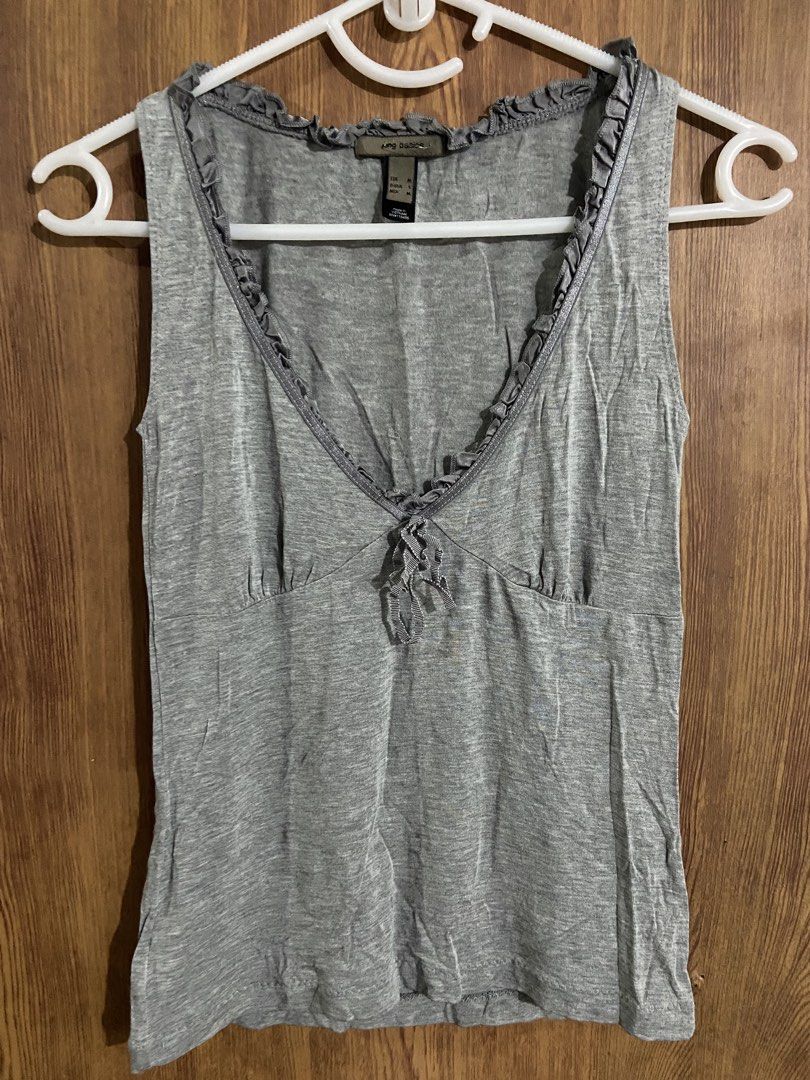MNG basics gray tank top with ruffled v-neck (Category: Sleeveless) located in Caloocan City. Submitted by lovedbyryu (Listing ID 1469459079, Image 1). Description: - Brand: MNG Basics - Color: Grey - Size: EUR M / D/USA S / MEX M - Material: Lightweight fabric, Made in Vietnam - Design: Sleeveless, V-neckline with ruffled trim and center tie detail - Condition/Quality: Clean neckline with neat stitching.