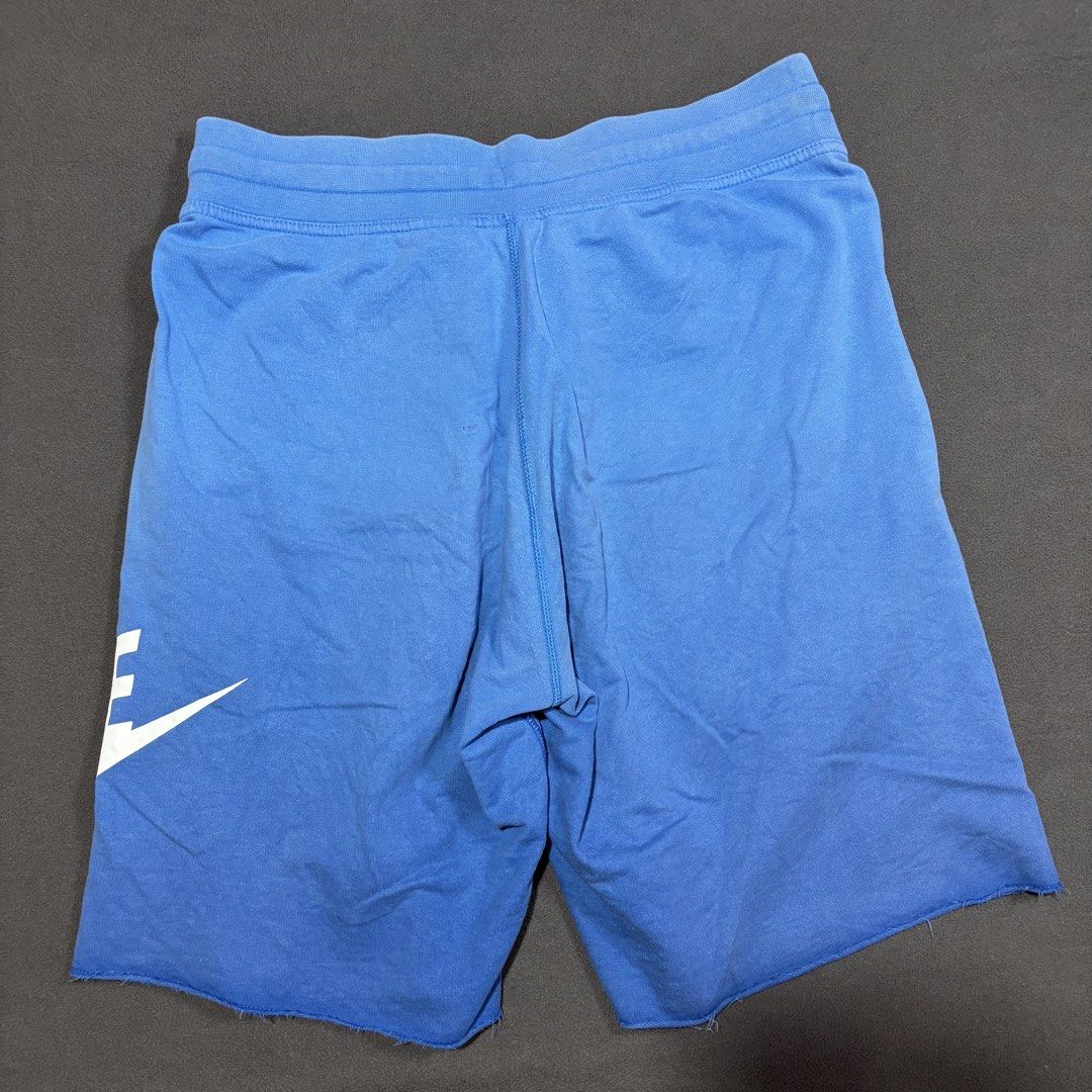 Nike Alumni Blue Raw Hem Sweatshorts (Category: Shorts) located in Mabalacat. Submitted by _limitlessfashion (Listing ID 1469411762, Image 2). Description: - Brand: Nike - Item: Sweatshorts - Color: Bright blue with a large vertical white Nike logo - Size: L (Tag attached) - Waist 32-34 - Length 21.5 - Hem 13 - Need wash only - Material: 100% cotton - Features: Elastic waistband with white drawstring cords, two side pockets, and a trendy raw hem 