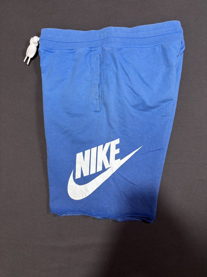 Nike Alumni Blue Raw Hem Sweatshorts (Category: Shorts) located in Mabalacat. Submitted by _limitlessfashion (Listing ID 1469411762, Image 3). Description: - Brand: Nike - Item: Sweatshorts - Color: Bright blue with a large vertical white Nike logo - Size: L (Tag attached) - Waist 32-34 - Length 21.5 - Hem 13 - Need wash only - Material: 100% cotton - Features: Elastic waistband with white drawstring cords, two side pockets, and a trendy raw hem 