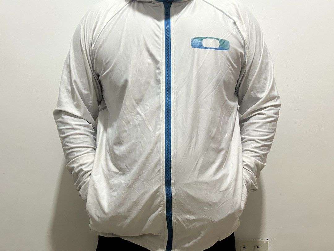 Oakley White Hooded Jacket Full Zip Size L (Category: Coats, Jackets and Outerwear) located in Manila. Submitted by andotputla37237 (Listing ID 1469515772, Image 1). Description: - Brand: Oakley - Style: Full-zip athletic hoodie - Size: Large (checked via neck tag) - Color: Crisp white with vibrant blue accents - Details: Blue zipper, blue logo graphic on left chest, attached hood, and two functional front pockets - Material: Lightweight, breatha