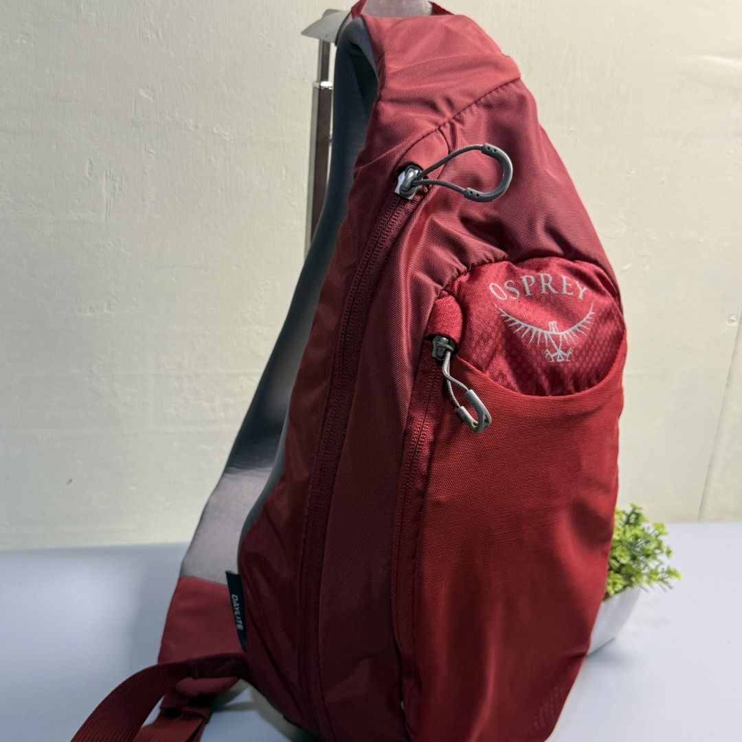 Osprey Daylite Sling Backpack Red Maroon (Category: Backpacks) located in Bago City. Submitted by g___shop (Listing ID 1469500560, Image 3). Description: - Brand: Osprey (Daylite Sling Bag) - Color: Red with grey patterned mesh details - Design: Compact teardrop shape with a sturdy, adjustable single strap and small buckle clip - Compartments: Front zippered pocket and spacious main compartment for everyday essentials - Comfort: Breathable grey b