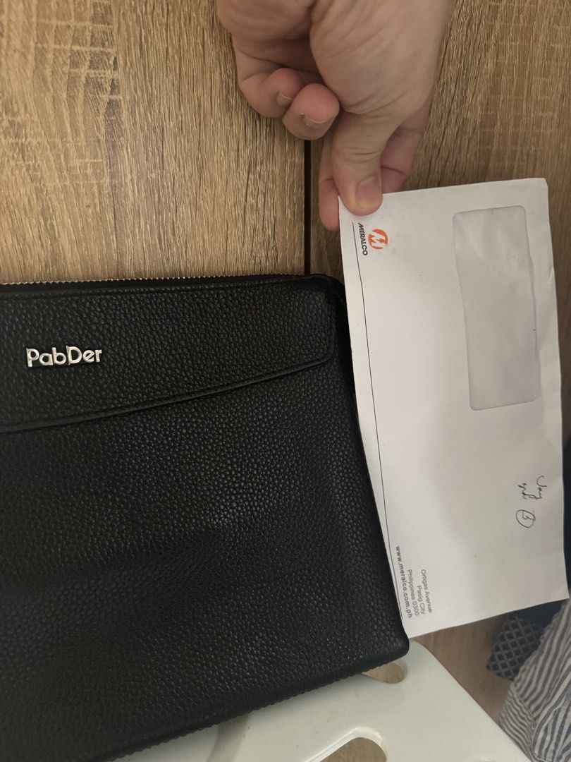 Men’s PabDer Black Leather Clutch Bag (Category: Belt bags, Clutches and Pouches) located in Mandaluyong City. Submitted by raykin (Listing ID 1469446312, Image 3). Description: Authentic black pebbled leather clutch from PabDer in clean condition. Features silver hardware, a secure top zip, a front flap pocket with a metal logo, and a brown-lined interior with an extra zip pocket. Please check the photos for the size reference against Meralco bi