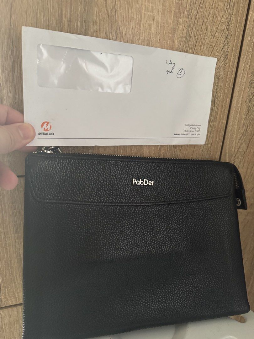 Men’s PabDer Black Leather Clutch Bag (Category: Belt bags, Clutches and Pouches) located in Mandaluyong City. Submitted by raykin (Listing ID 1469446312, Image 2). Description: Authentic black pebbled leather clutch from PabDer in clean condition. Features silver hardware, a secure top zip, a front flap pocket with a metal logo, and a brown-lined interior with an extra zip pocket. Please check the photos for the size reference against Meralco bi