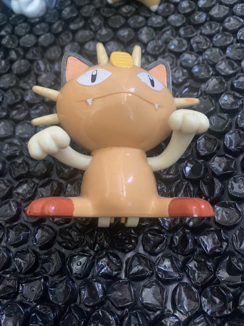 Pokemon Meowth plastic figure toy (Category: Figurines & Statues) located in Manila. Submitted by emenem.m (Listing ID 1469421393, Image 1). Description: - Character: Meowth from Pokemon - Design: Brown body, cream paws, orange feet, iconic gold coin on head, black-tipped ears, and whiskers - Pose: Classic raised paws - Size: Standard mini figure - Condition: Good, with minor paint scuff marks from storage - Note: A great addition to any Pokemon 