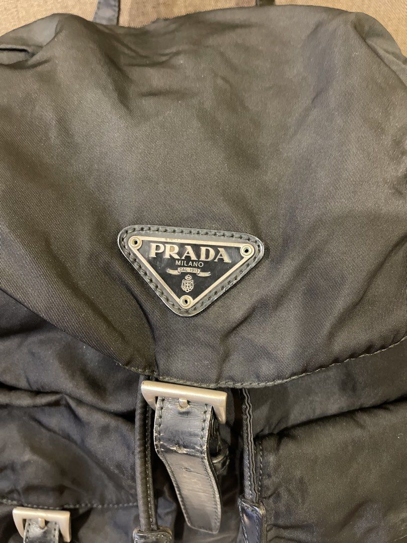 Prada Black Nylon Backpack (Category: Backpacks) located in Manila. Submitted by jnjsluxury (Listing ID 1469455117, Image 2). Description: - Brand: Prada - Material: Classic black nylon with leather trim - Logo: Iconic metal triangle logo plate - Closure: Drawstring under flap with secure buckle straps - Pockets: Two exterior pockets for easy access - Straps: Adjustable black webbed shoulder straps and top handle - Condition: heavily used with fl