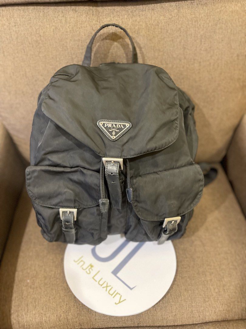 Prada Black Nylon Backpack (Category: Backpacks) located in Manila. Submitted by jnjsluxury (Listing ID 1469455117, Image 1). Description: - Brand: Prada - Material: Classic black nylon with leather trim - Logo: Iconic metal triangle logo plate - Closure: Drawstring under flap with secure buckle straps - Pockets: Two exterior pockets for easy access - Straps: Adjustable black webbed shoulder straps and top handle - Condition: heavily used with fl