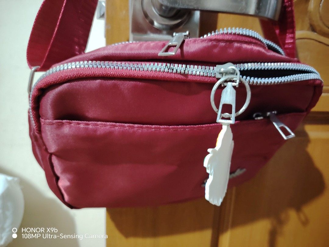 Red Shoulder Bag with Zipper Pockets (Category: Shoulder Bags) located in Manila. Submitted by justybelieve2026 (Listing ID 1469451778, Image 3). Description: - Vibrant red nylon-feel material with a durable build - Secure main zipper closure to keep your belongings safe - Convenient front zip pocket featuring a stylish metal pull tab - Elegant silver-tone brand logo plate on the lower right corner - Adjustable strap on both sides for a customize