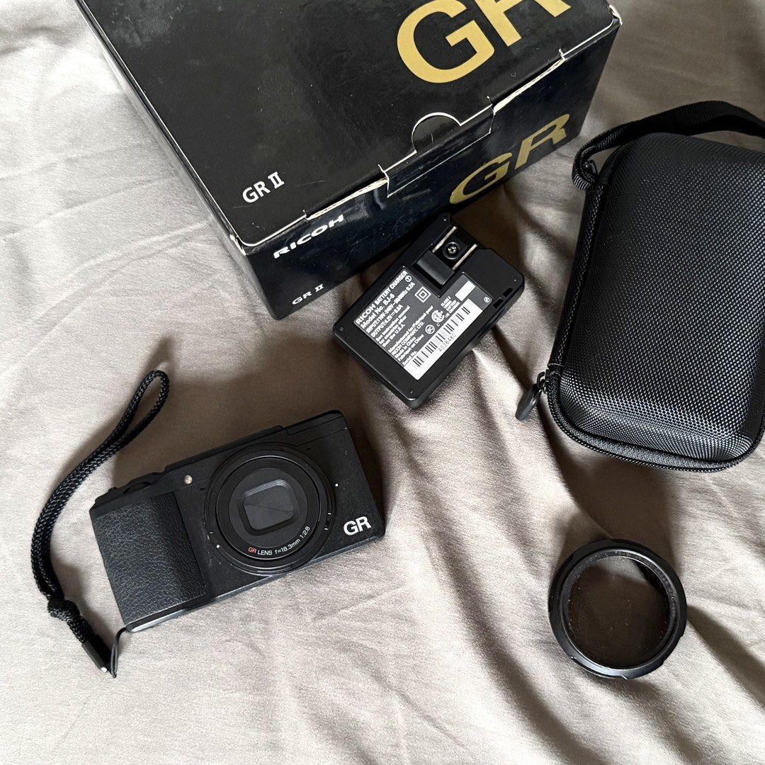 RUSH Ricoh GR II with Box and Accessories (Category: Cameras) located in Pasig City. Submitted by patrik_ (Listing ID 1469421890, Image 1). Description: - Camera: Ricoh GR II compact camera, fully functional and ready for street photography. - Bought in 2019 - 3,155 shutter count only - Included Accessories: Original box, battery charger, protective case, wrist strap, and lens hood and clear filter. - Condition Notes: Missing lens ring Scratch ne