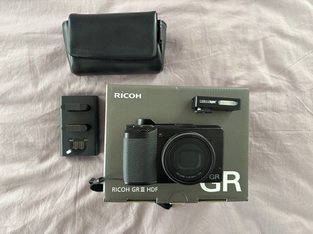 Ricoh GR III HDF Digital Camera with Accessories (Category: Cameras) located in Quezon City. Submitted by chinchiminni (Listing ID 1469426803, Image 1). Description: - Camera: Ricoh GR III HDF compact camera (includes original box) - Condition: Clean body with minimal signs of handling - Accessories included: Dual battery charger, black leather case, thumb grip attachment, and Medalight mini flash unit - Extra: Wrist strap securely attached - Hig