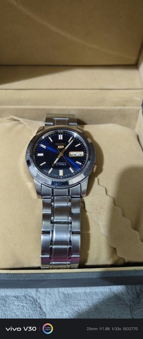 Seiko 5 Automatic 21 Jewels Blue Dial Watch (Category: Men's Watches) located in Taguig. Submitted by thrifthub.ph (Listing ID 1469443944, Image 3). Description: - Brand: Seiko 5 Automatic - Dial: Striking blue sunburst face with gold-tone hands and hour markers - Features: Day and date window at the 3 o'clock position, crown at 4 o'clock - Material: Durable stainless steel case and bracelet - Inclusions: Comes with the original watch box as show