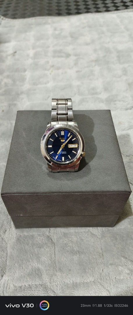 Seiko 5 Automatic 21 Jewels Blue Dial Watch (Category: Men's Watches) located in Taguig. Submitted by thrifthub.ph (Listing ID 1469443944, Image 2). Description: - Brand: Seiko 5 Automatic - Dial: Striking blue sunburst face with gold-tone hands and hour markers - Features: Day and date window at the 3 o'clock position, crown at 4 o'clock - Material: Durable stainless steel case and bracelet - Inclusions: Comes with the original watch box as show