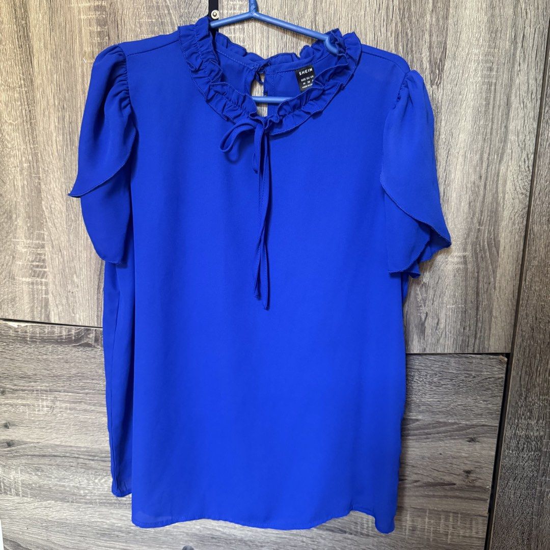 SHEIN Royal Blue Ruffle Neck Blouse Size M (Category: Blouses) located in Bacolod City. Submitted by hannacampsss (Listing ID 1469404833, Image 1). Description: - Brand: SHEIN - Color: Bright Blue - Size: Medium (EU 38, US 6) - Design: Ruffle collar with front tie string, short ruffled sleeves, and back keyhole button closure - Material: Lightweight and comfortable fabric - Styling: Easy to match with jeans or skirts.