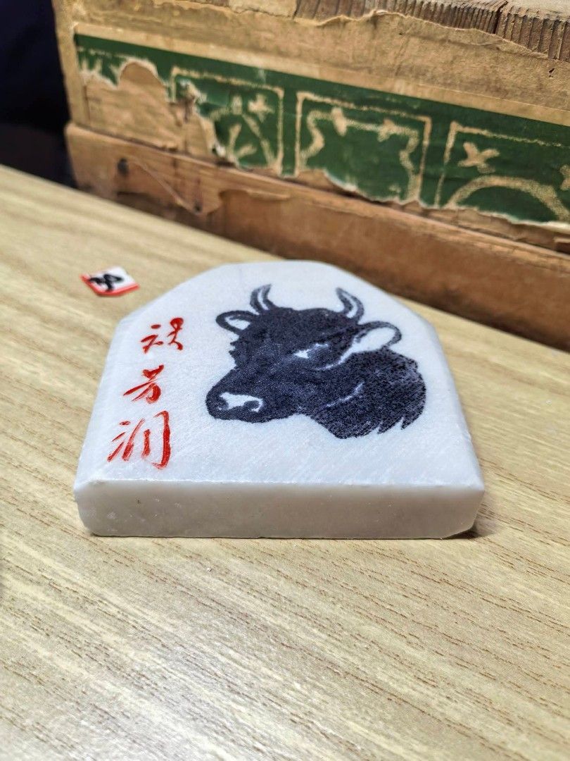 Stone Ox Carving Plaque (Category: Other Home Decor) located in Cebu City. Submitted by dudes_villanueva (Listing ID 1469431568, Image 3). Description: Japanese Marble / Stone Ox Carving Plaque ​Hand-carved and polished white stone/marble plaque featuring a detailed black bull/ox graphic and red Japanese calligraphy characters on the front. The back features blue handwritten markings (60.6.24 土産), indicating it was acquired as a souvenir or gift 