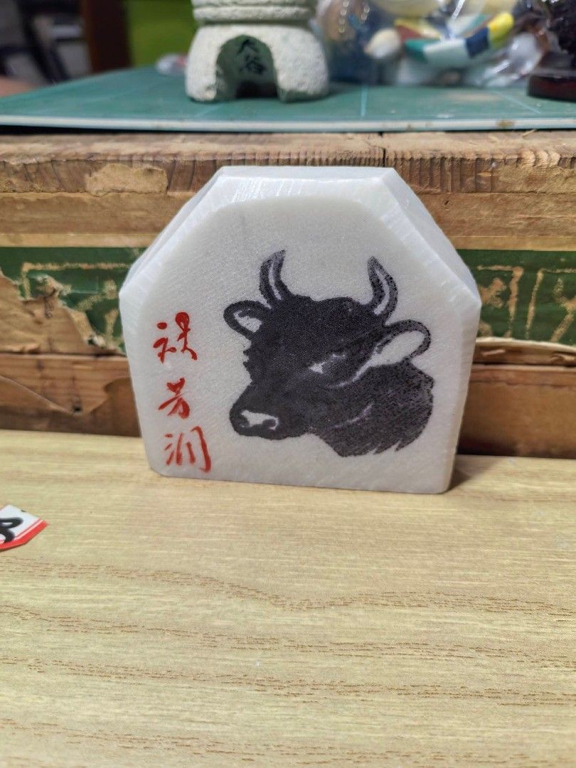 Stone Ox Carving Plaque (Category: Other Home Decor) located in Cebu City. Submitted by dudes_villanueva (Listing ID 1469431568, Image 2). Description: Japanese Marble / Stone Ox Carving Plaque ​Hand-carved and polished white stone/marble plaque featuring a detailed black bull/ox graphic and red Japanese calligraphy characters on the front. The back features blue handwritten markings (60.6.24 土産), indicating it was acquired as a souvenir or gift 