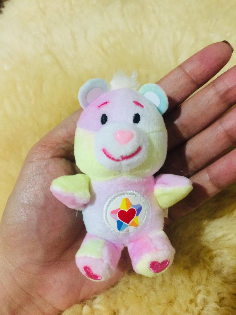 Super Impulse Care Bears Care Bears Togetherness Bear (Category: Plushies & Soft Toys) located in Baguio. Submitted by izza_thrifty (Listing ID 1469567597, Image 2). Description: - Authentic Mini Togetherness Bear plush toy with original tag (2023) - Pastel tie-dye multicolored fur with star and rainbow belly badge - Sweet pink embroidered heart on the foot and red heart on the back - Tiny, portable size that fits right in the palm of your hand -