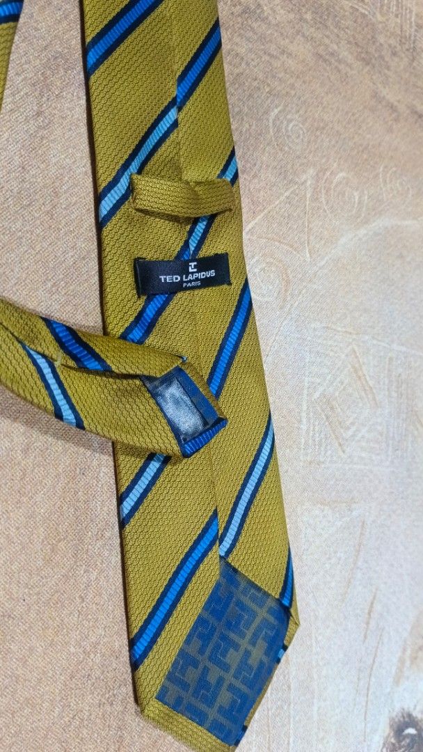 Ted Lapidus Paris Striped Necktie Yellow Blue (Category: Ties) located in Cavite. Submitted by navias (Listing ID 1469395936, Image 2). Description: Origin:UAE100% - Brand: Ted Lapidus Paris - Color/Pattern: Mustard yellow with diagonal blue and light blue stripes - Material: Textured woven fabric with branded back keeper loop - Width: Standard blade - Occasion: Ideal for formal wear, office outfits, and business meetings Transaction Details: -vi