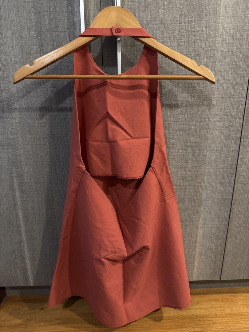 Terracotta Halter Neck Dress Open Back (Category: Dresses) located in Makati City. Submitted by kkk.shops (Listing ID 1469512151, Image 2). Description: - Color: Terracotta orange - Style: Minimalist halter neck dress - Design: Open back with nape button closure - Silhouette: Structured, widens towards the hem - Length: Above the knee - Condition: Excellent, clean fabric with no stains or damage.