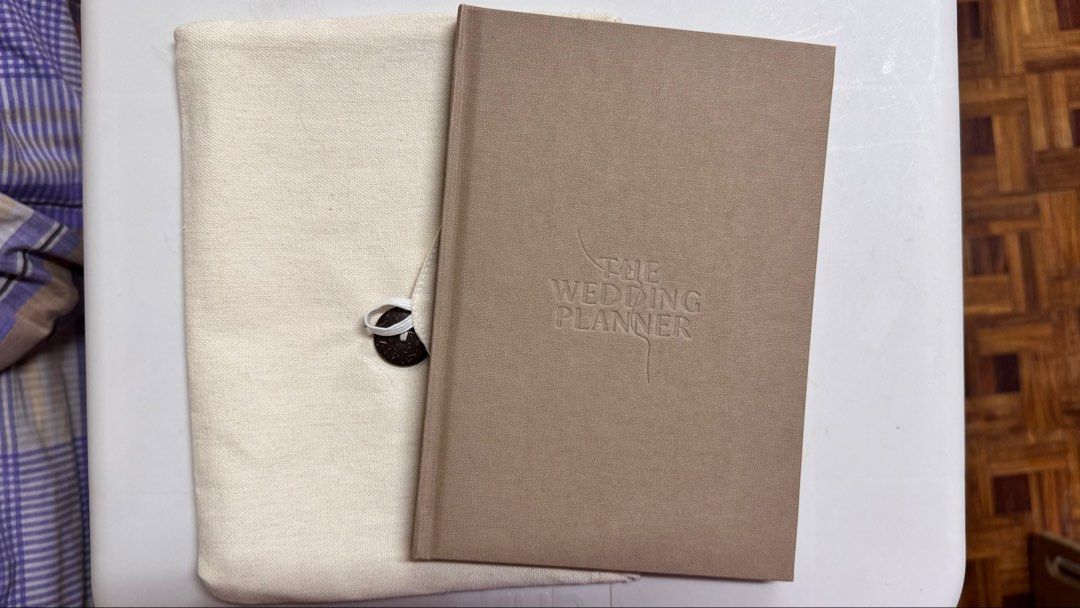 The Wedding Planner Book with Pouch (Category: Storybooks) located in Manila. Submitted by fcloset24 (Listing ID 1469465681, Image 1). Description: - Elegant beige fabric hardcover wedding planner - Includes a matching canvas drawstring pouch with button closure - Structured sections for venues, dress styles, and shoe planners - Blank monthly calendar layouts for easy scheduling - Plenty of blank pages for notes and organizing your big day.