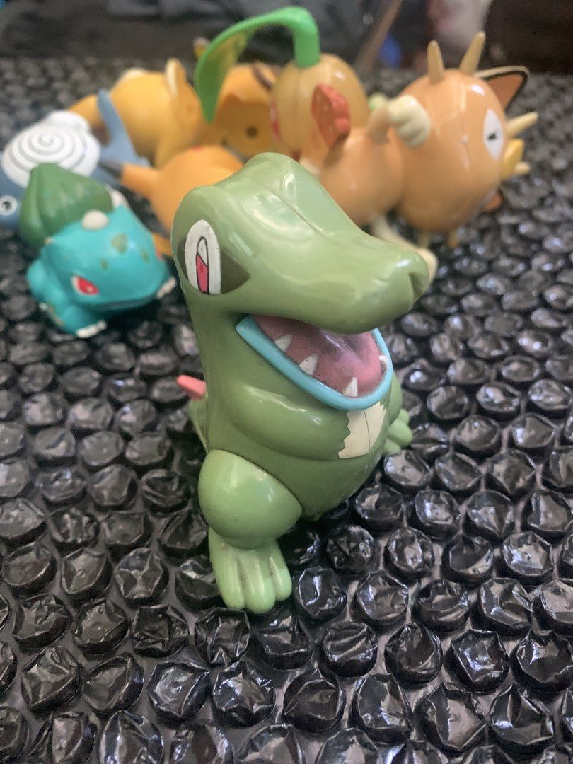 Totodile Pokemon toy figure (Category: Figurines & Statues) located in Manila. Submitted by emenem.m (Listing ID 1469421693, Image 1). Description: - Item: Green Totodile Pokemon figurine - Details: Stands upright, pink spikes, blue tongue out, official Nintendo copyright stamp on bottom - Size: Measures a few cm tall - Condition: Minor scuff marks from previous play and handling - Note: Great for collectors; other figures in background are not i