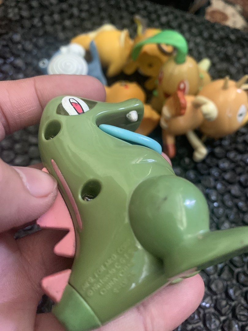 Totodile Pokemon toy figure (Category: Figurines & Statues) located in Manila. Submitted by emenem.m (Listing ID 1469421693, Image 2). Description: - Item: Green Totodile Pokemon figurine - Details: Stands upright, pink spikes, blue tongue out, official Nintendo copyright stamp on bottom - Size: Measures a few cm tall - Condition: Minor scuff marks from previous play and handling - Note: Great for collectors; other figures in background are not i